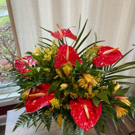 Red anthuriums and yellow flowers in a glass vase
