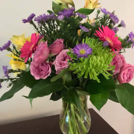 Mixed bouquet of pink roses, gerbera daisies, and purple flowers in a glass vase