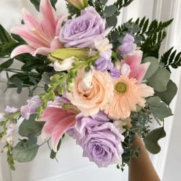 Handheld bouquet of pink lilies, lavender roses, and peach gerbera daisies