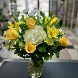 Yellow roses and lilies arranged with white hydrangea in a glass vase