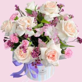 Pink and white roses arranged in a striped hat box with a purple ribbon