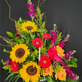 Colorful arrangement of sunflowers, orange roses, and hot pink gerbera daisies in a low white container.