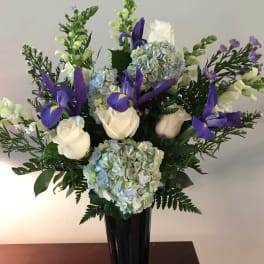 White roses and blue hydrangeas with purple irises in a tall vase