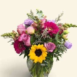 Mixed bouquet in a glass vase with sunflowers, roses, and pink gerberas