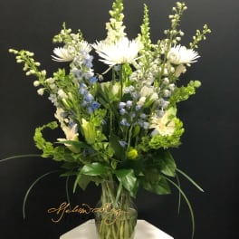 Tall white and blue floral arrangement in a clear glass vase