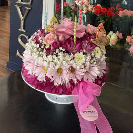 Pink floral arrangement with roses, daisies, and candles in a white pedestal bowl