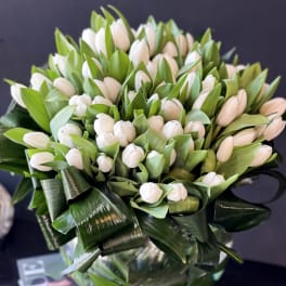 Bouquet of white tulips with broad green leaves in a glass vase