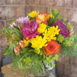 Mixed bouquet of yellow, purple, and orange flowers in a glass vase