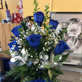 Blue roses arranged with baby's breath and greenery in a vase.