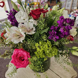 Mixed bouquet of pink and red roses, white blooms, and purple flowers in a clear glass vase