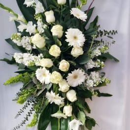 Tall white floral standing spray on an easel with gerberas, roses, and gladiolus