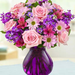 Pink roses and purple daisies in a purple glass vase