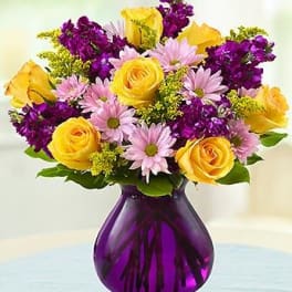 Yellow roses and lavender daisies in a purple vase