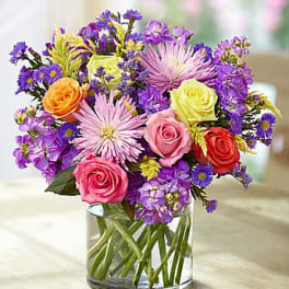 Mixed bouquet of roses and purple flowers in a clear glass vase
