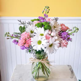 Mixed bouquet of white daisies, pink roses, and purple flowers in a glass vase