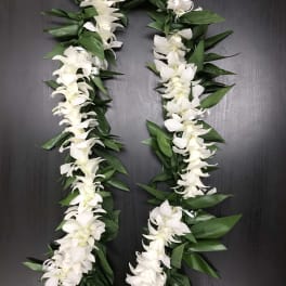 White orchid lei with green leaves on a dark surface