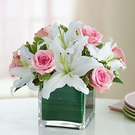 Pink roses and white lilies arranged in a clear square vase