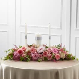 Pink rose centerpiece with three white candles on a table