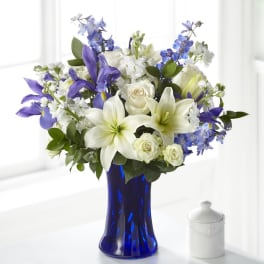White lilies, roses, and blue-purple flowers in a cobalt vase