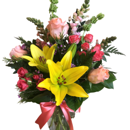 Bouquet of yellow lilies and pink roses in a glass vase with a pink ribbon