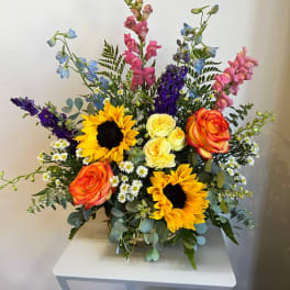 Colorful mixed bouquet with sunflowers, roses, and tall blue and pink blooms in a vase
