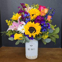 Colorful bouquet with sunflowers, roses, lilies, and a white vase