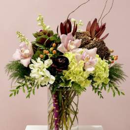 Mixed floral arrangement in a clear glass vase with pink orchids and green hydrangeas