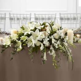 White floral centerpiece with lilies and candles on a table