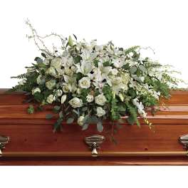 White floral casket spray with roses and lilies on a wooden casket