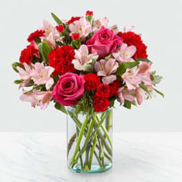 Bouquet of pink roses, red carnations, and pale pink alstroemeria in a glass vase