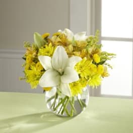 White lilies and yellow flowers in a clear glass vase