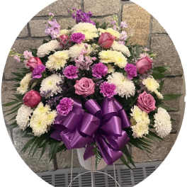 Pink and white floral spray with a purple ribbon bow in a white stand