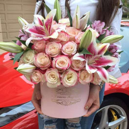 Round pink hatbox of cream roses and pink lilies held in front of a red car