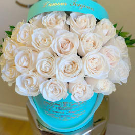 White roses arranged in a turquoise hatbox with gold lettering.