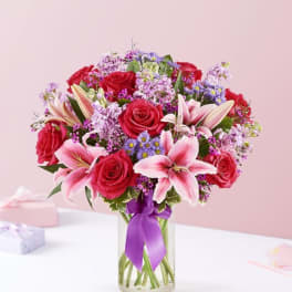 Bouquet of red roses and pink lilies in a glass vase with a purple ribbon