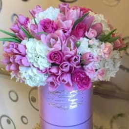 Pink tulips and roses with white hydrangeas arranged in a lavender round hatbox.
