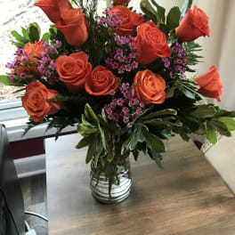 Orange roses and purple filler flowers in a clear glass vase