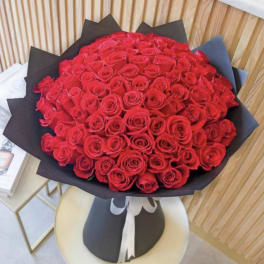 Large bouquet of tightly clustered red roses wrapped in black paper and tied with a white ribbon
