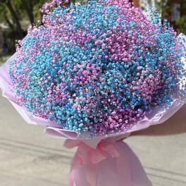 Large round bouquet of blue and pink tiny blooms wrapped in pale pink paper with a bow