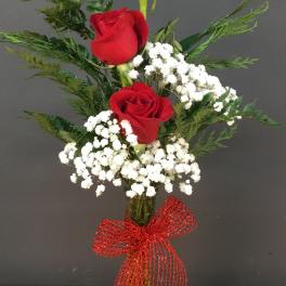 Three red roses in a clear vase with white baby's breath and a red bow