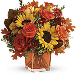 Autumn bouquet of orange roses and yellow sunflowers in a square glass vase