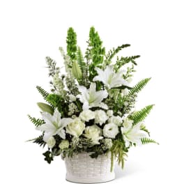 Tall white lilies, roses, and carnations arranged in a white woven basket