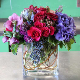 Bouquet of red roses, purple hydrangeas, and pink blooms in a clear square vase