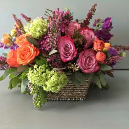 Mixed bouquet of roses and purple flowers in a woven basket