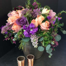 Mixed bouquet of peach roses and purple flowers in a dark vase