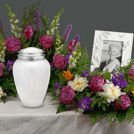 Funeral urn surrounded by purple, white, and orange flowers with a framed portrait