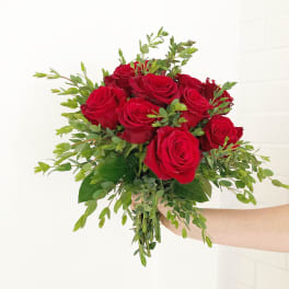 Hand-tied bouquet of red roses with lush green foliage held against a white background