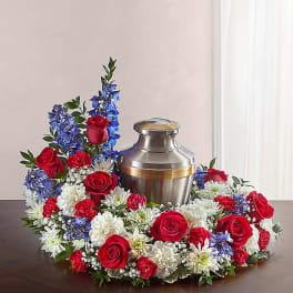 Floral wreath with red roses, white daisies, and blue flowers around a silver urn