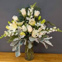 White lilies and roses arranged in a glass vase with silver foliage