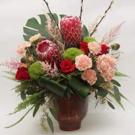 Tropical bouquet with red protea, roses, and carnations in a brown vase